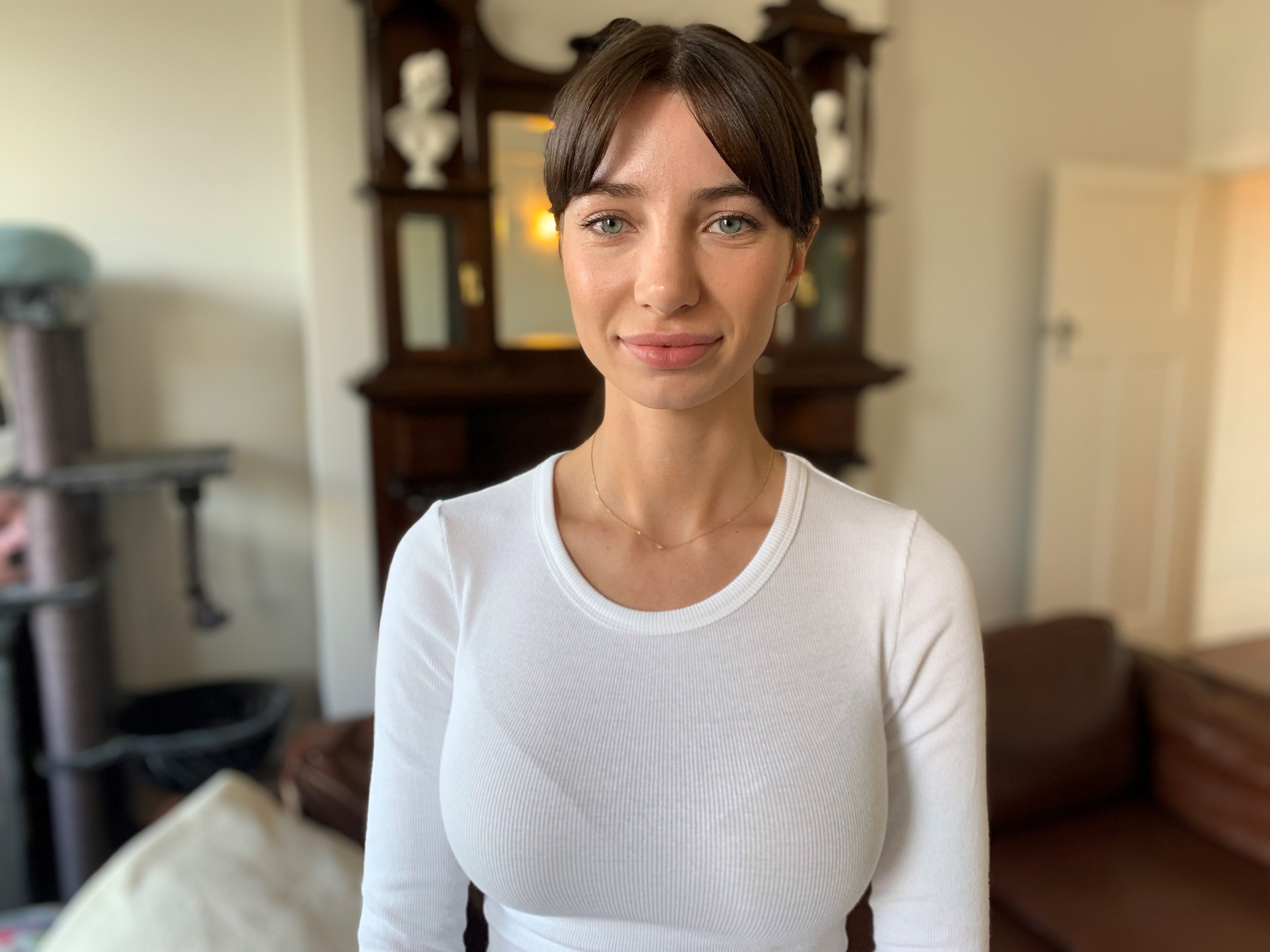 A woman stands in a room at home wearing a white top.