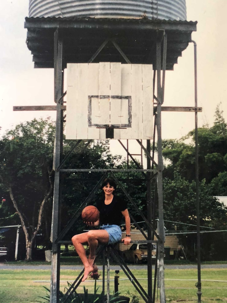 A woman sits on a metal ledge underneath a basketball backboard