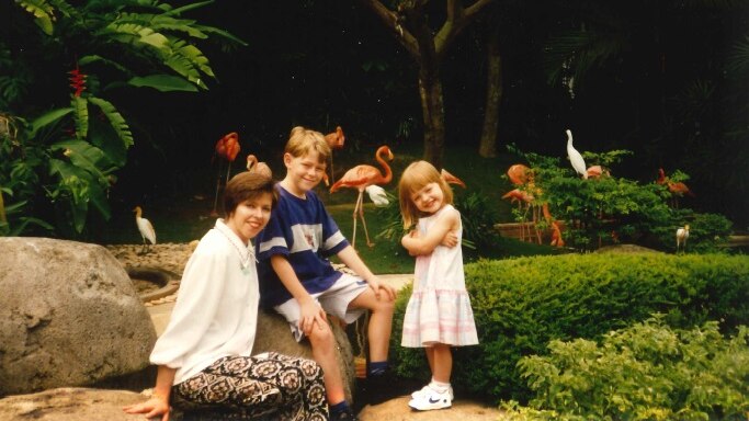 Judi Green and her two children sitting in a park, with plastic flamingos in the background.