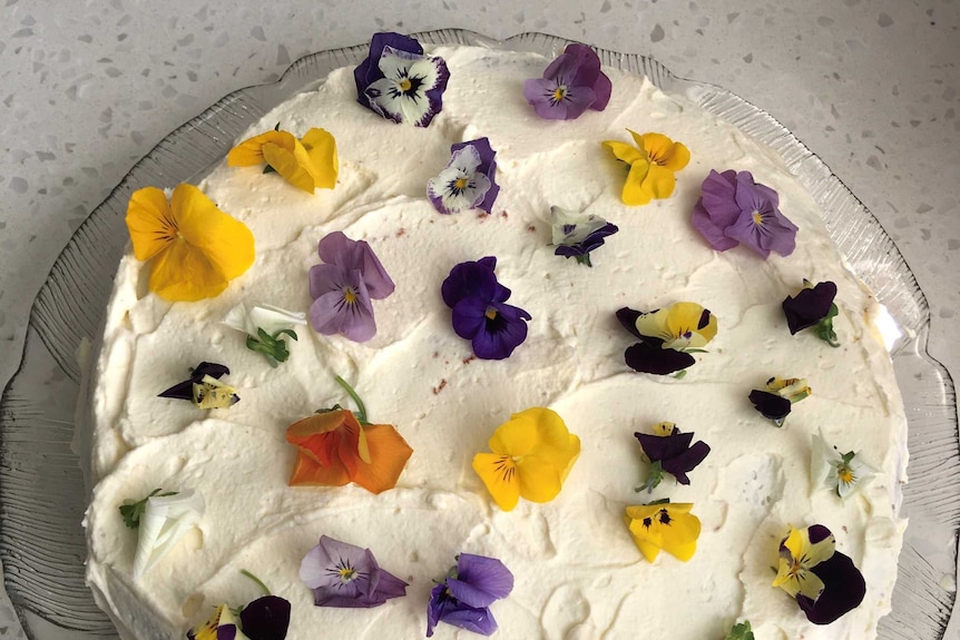 A lemon cake iced with cream and decorated with edible flowers, a simple wedding cake for five.