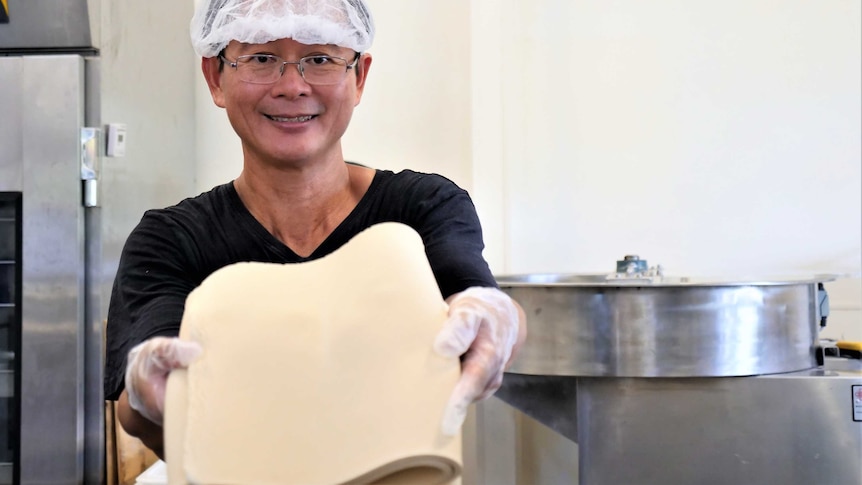 Shing Hee Ting holding a mat of flattened dough in the noodle making process
