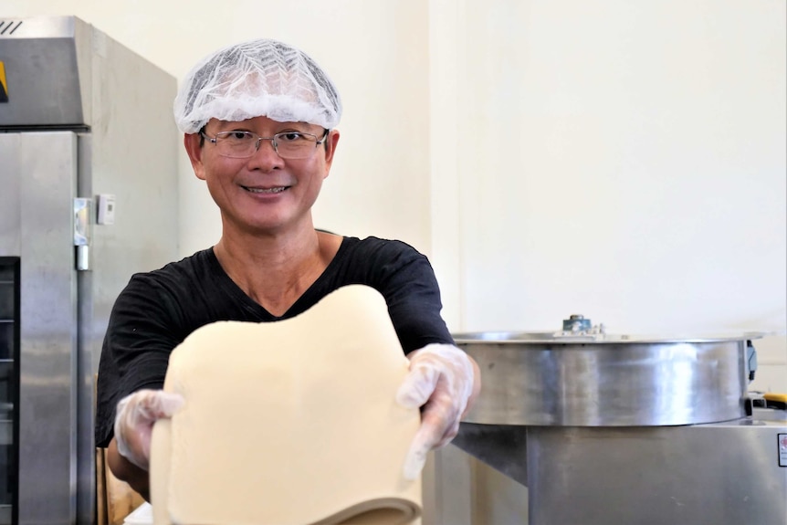 Shing Hee Ting holding a mat of flattened dough in the noodle making process