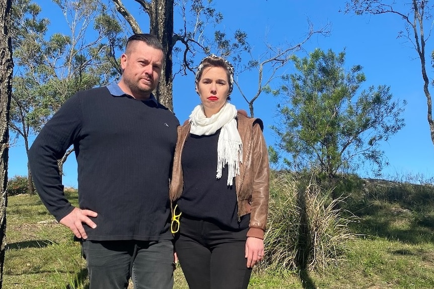 A man and a woman stand on a tree covered hill.