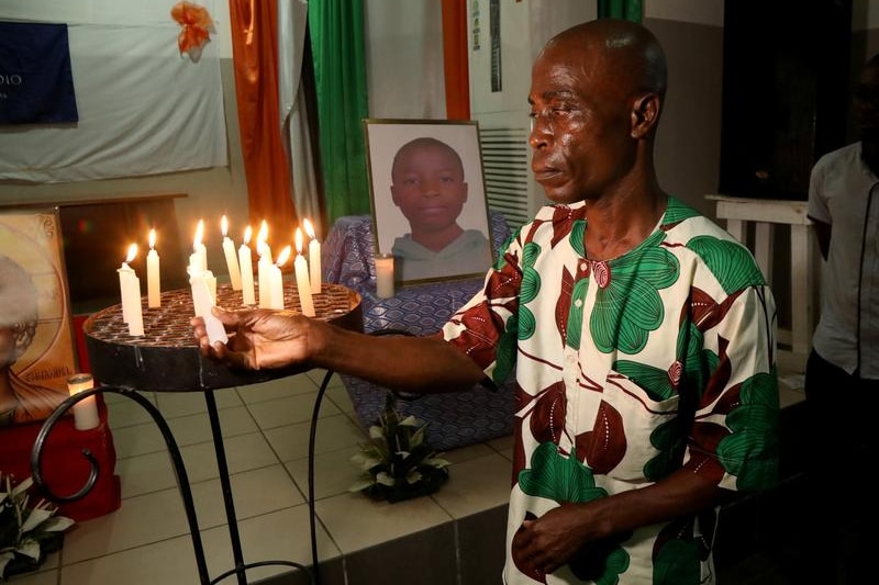 A man lightening a candle at a tribute prayer, a picture of the dead boy is in the background.