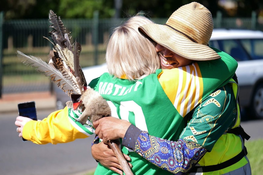 Alwayn Doolan smiles and wraps his arms around Cara Bartlett, while holding his message stick.