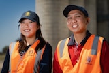 A young man and woman in high-vis vests labelled 'GrainCorp' stand smiling in front of a grain silo.