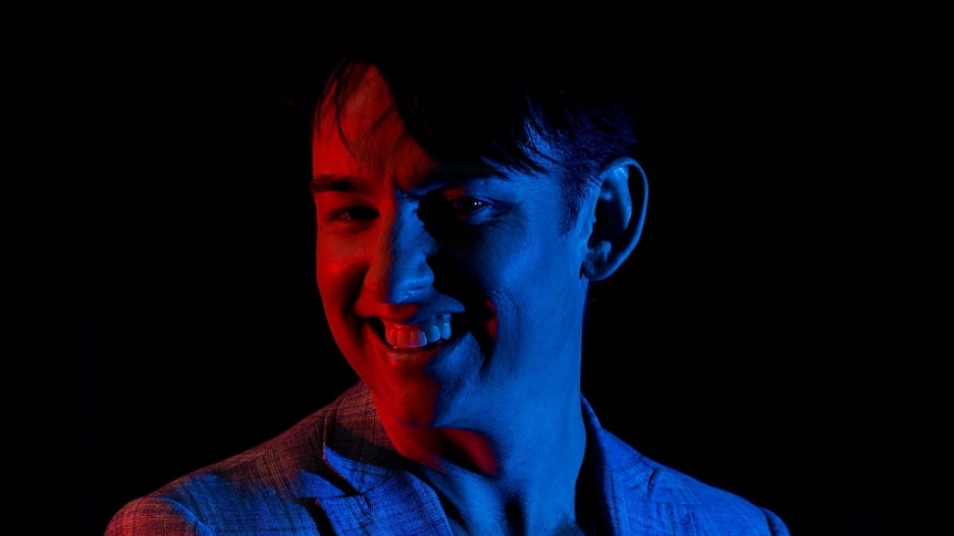 A man in a jacket is lit by a red and blue lights