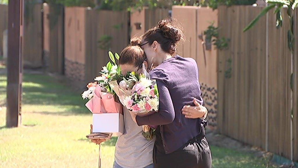 Two women holding flowers hug one another