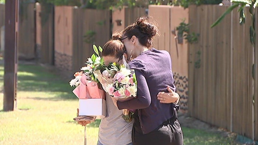Two women holding flowers hug one another