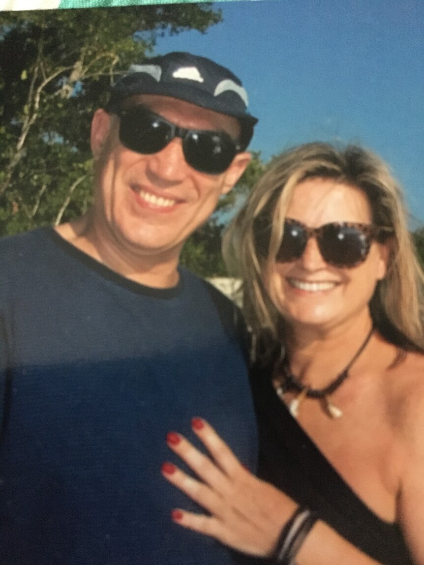 Karyne Moraitis and her husband smiling in a photo, underneath a blue sky.