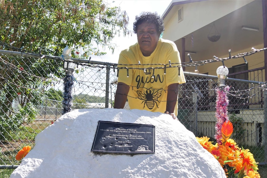 Aboriginal woman stares at the camera as she stands above her brother's decorated memorial rock