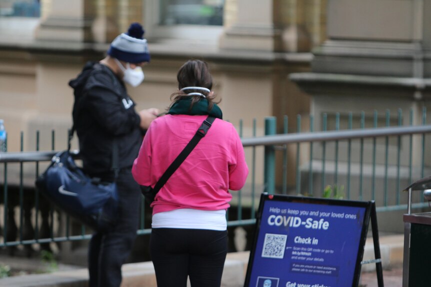 Two people rugged up in warm clothing, wearing face masks outside a hospital.