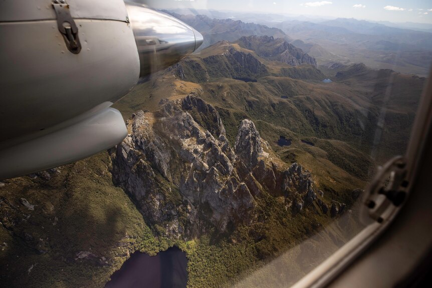 A rocky mountain top and lake viewed from above, through an aeroplane window