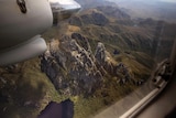 A rocky mountain top and lake viewed from above, through an aeroplane window