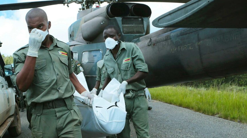 Zimbabwe military personnel carry the body of someone who died in Cyclone Idai from a helicopter. They are wearing masks.