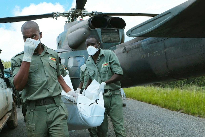 Zimbabwe military personnel carry the body of someone who died in Cyclone Idai from a helicopter. They are wearing masks.