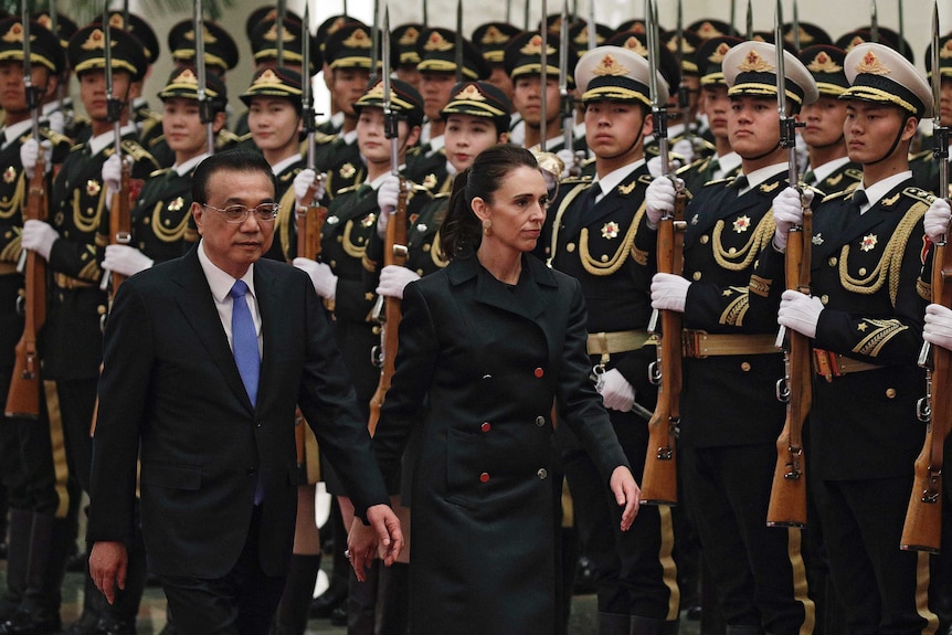 New Zealand Prime Minister Jacinda Ardern and Chinese Premier Li Keqiang walk with a crowd of uniformed guards holding bayonets'