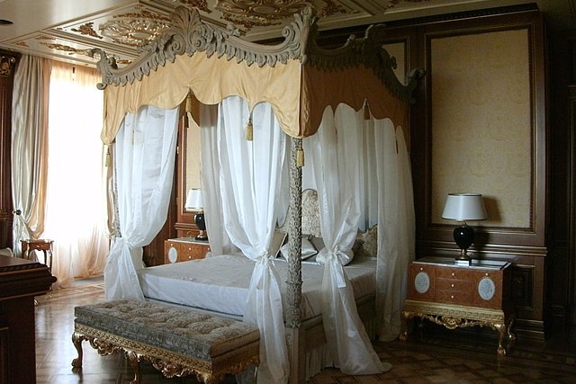 An opulent four poster bed with a golden canopy in a huge bedroom 