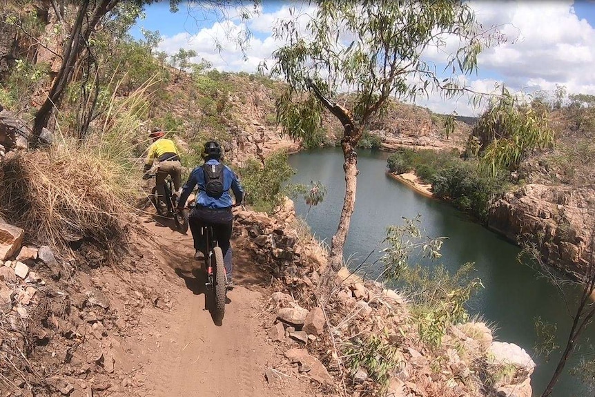 Two mountain bikers shot from behind riding along a dramatic scenic path high up a steep gorge