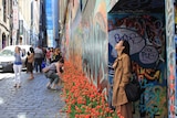 A woman stands in Melbourne's Hosier Lane surrounded by tulips and people taking photos.