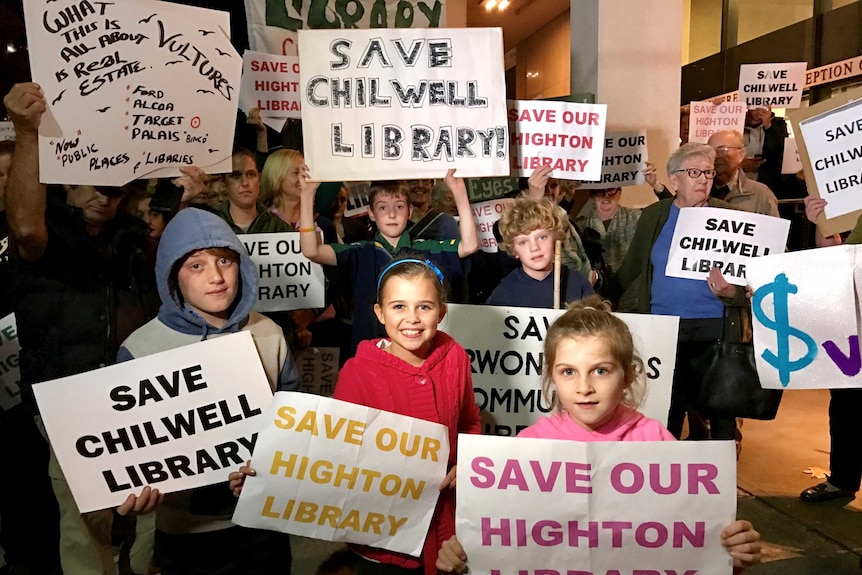 A group of children hold signs and banners saying 'save our library'.