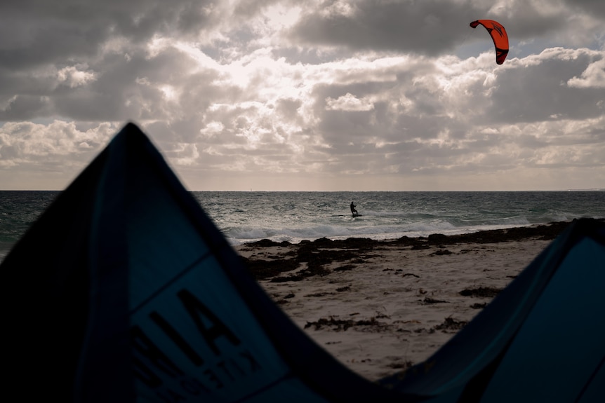 A kitesurfer on the water at Pinnaroo Point with tents in shadows in the foreground and the sun peeking through clouds above.