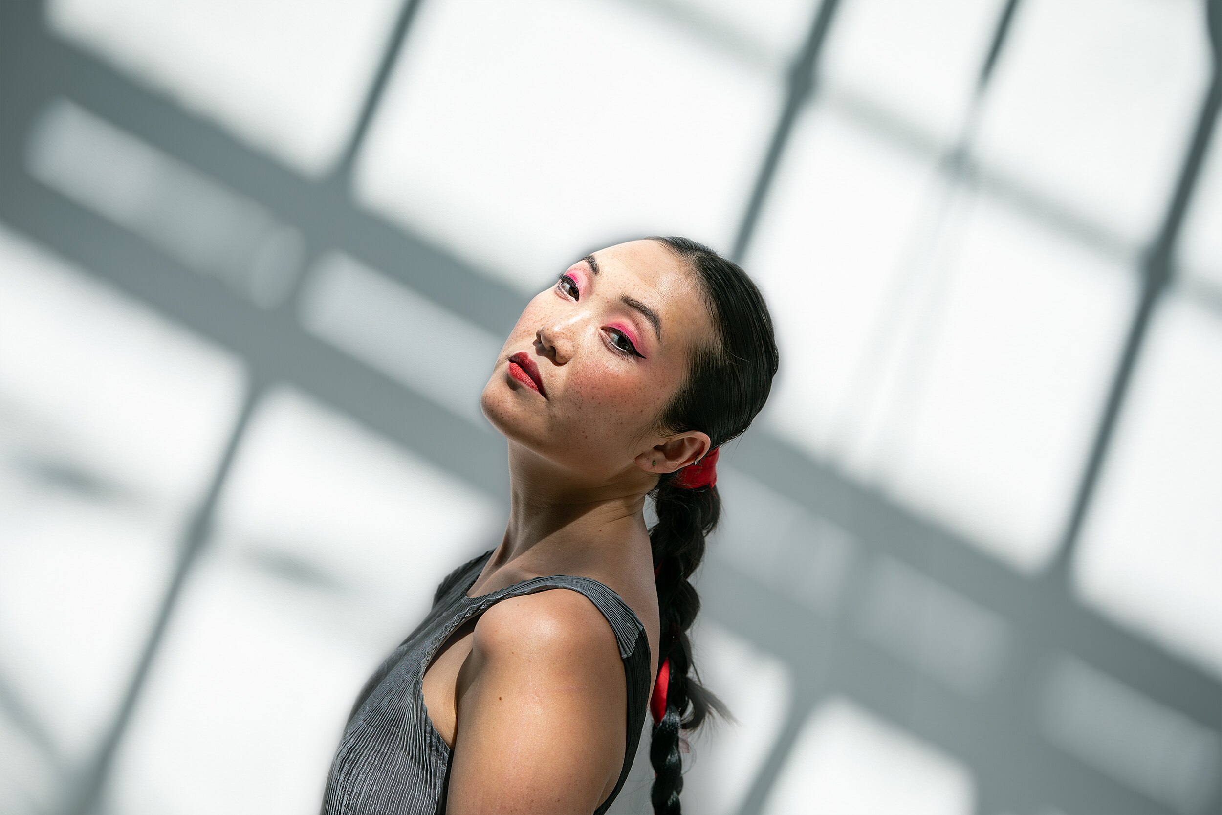 A Chinese Australian woman in her 30s wears a silver dress and stands in dappled sunlight against a white wall.