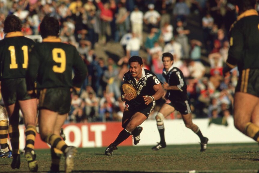 Olsen Filipaina in a black and white NZ jersey runs at some Kangaroos player wearing green and gold jerseys.