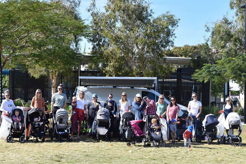 A line of mothers with their children in prams in a park.