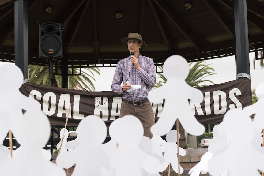 A man with a microphone and a hat addressing a crowd holding 