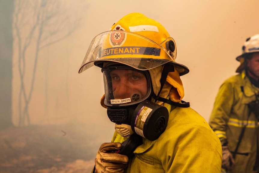 A firefighter wears a mask with smoke haze in the background.