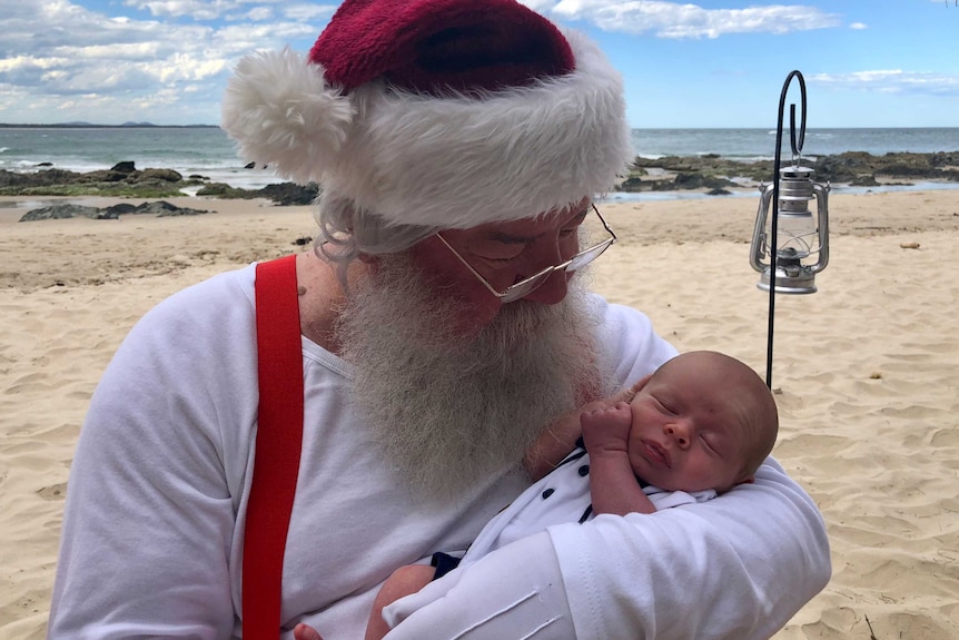 Santa on the beach holding a baby.