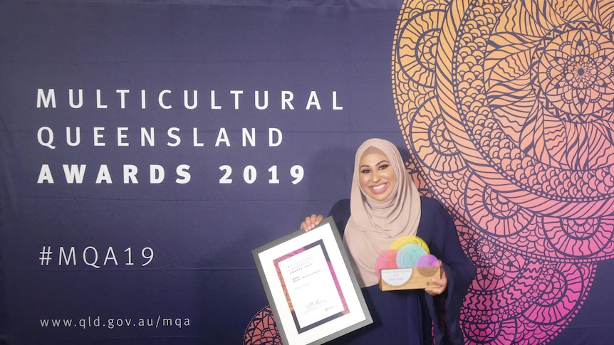 Nadia Saeed holds an award in front of a sign saying Multicultural Queensland Awards 2019.