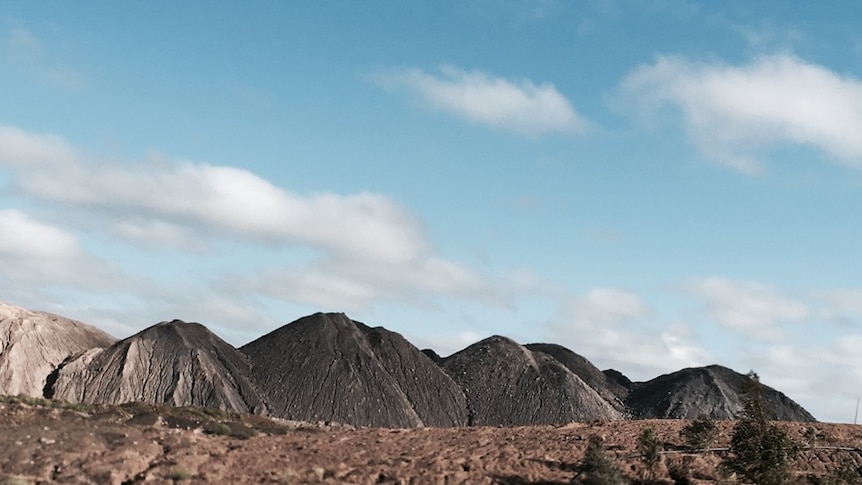 Discarded piles of waste coal rise up from the flat, barren landscape outside a Central Queensland mining town