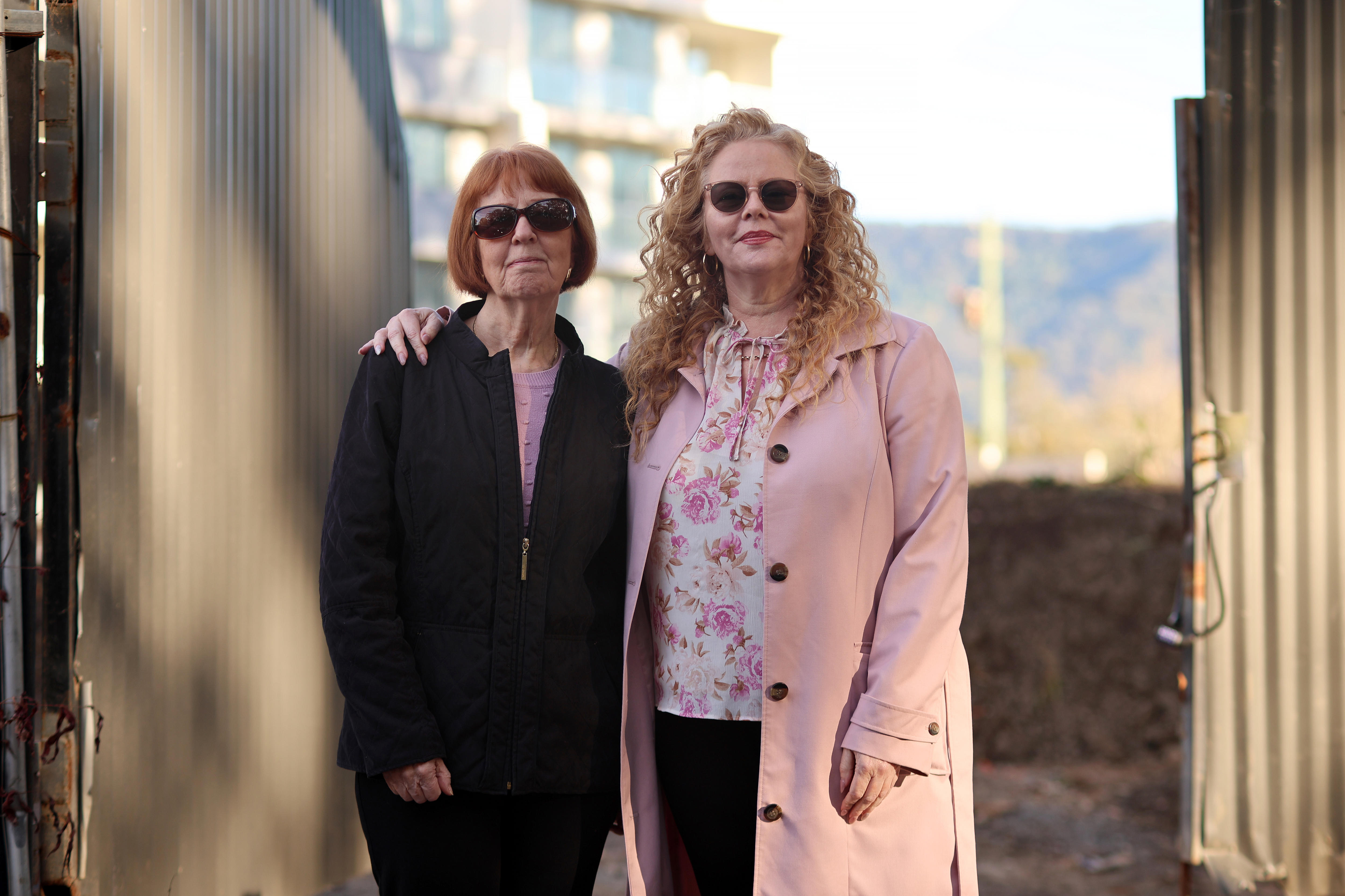 two women, one with blonde curly hair and one with a red bob, stand in front of a construction site