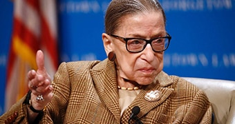 Ruth Bader Ginsburg raises her hand while speaking.