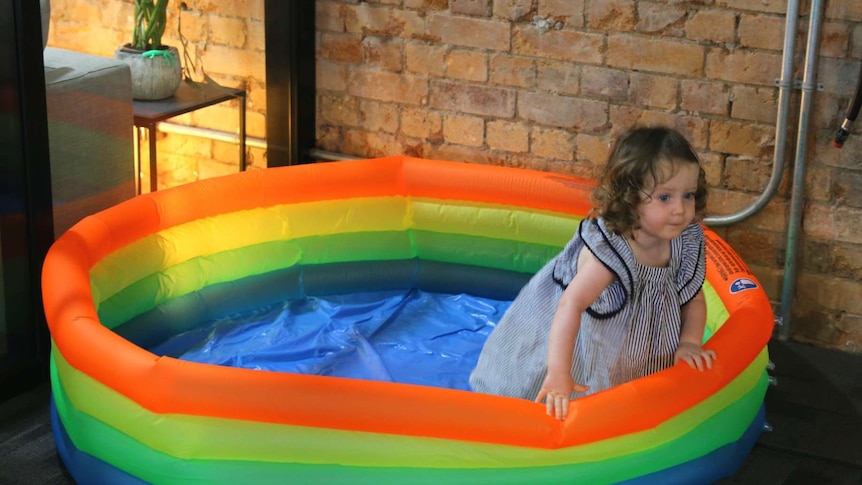 A small girl playing in a blow-up pool.