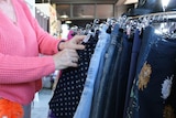 A woman browses through a rack of skirts.