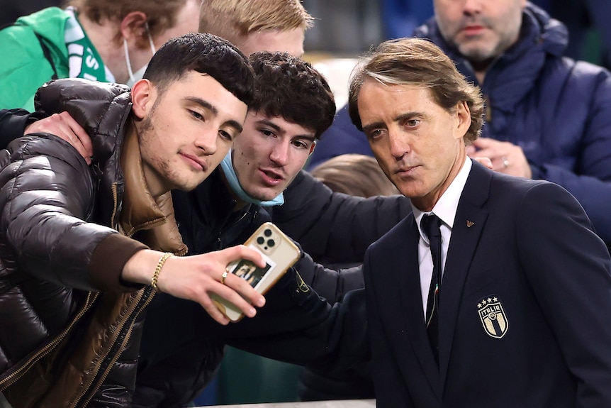 An Italian football fan uses his mobile phone to take a selfie of him, his friend and the Italian football coach. 