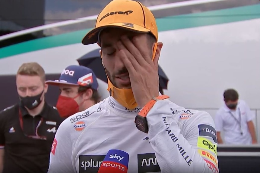 Daniel Ricciardo wipes sweat away as he faces the media.