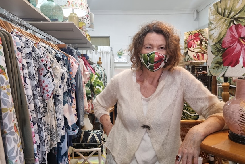 Woman stands beside a rack of clothes while wearing a floral facemask