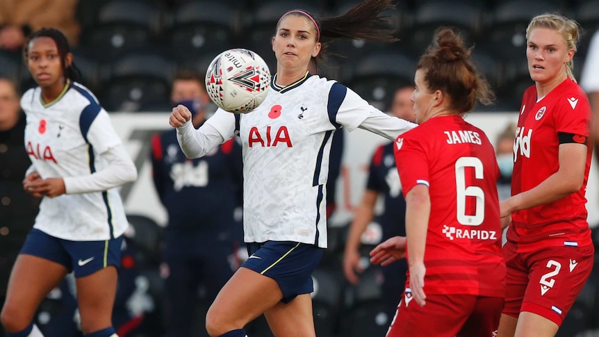 A women's soccer player eyes the bouncing ball as her opponents close in.