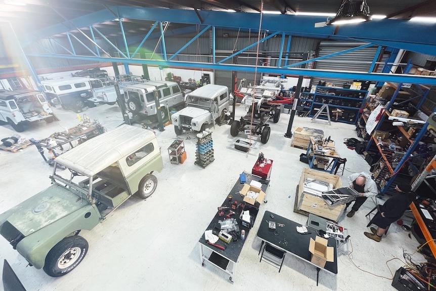 A bird's-eye view of an automotive workshop with various classic cars being worked on