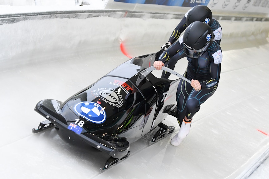 Bree Walker and Sarah Blizzard push a bobsled on the ice.