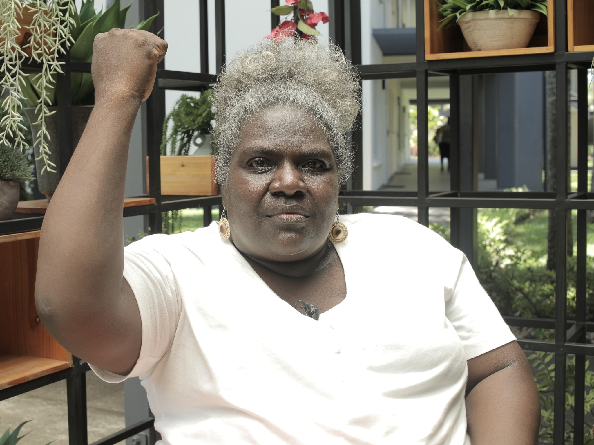 A Solomon Islands woman sitting in a bright cafe raising her right arm in solidarity expression 