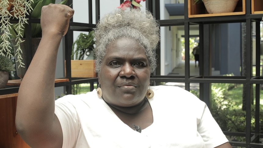 A Solomon Islands woman sitting in a bright cafe raising her right arm in solidarity expression 