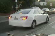 A photo of a white sedan taken from behind driving along tram tracks on a Melbourne street.