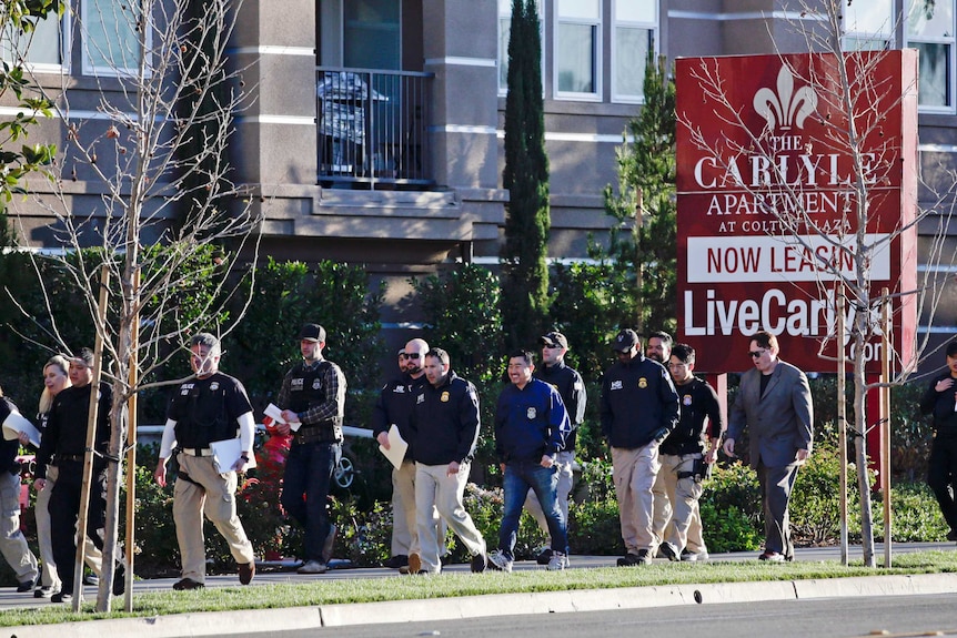 Up to 16 federal officers walk on the footpath with a brown apartment block seen in the background.