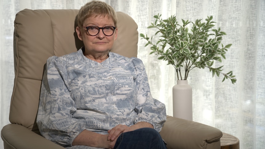 A woman with glasses sitting in an armchair next to a plant