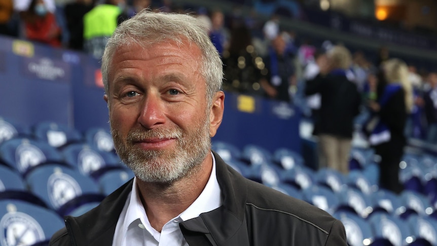 A bearded man wearing a jacket stands in the grandstand after the team he owns, Chelsea, wins the Champions League.